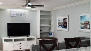 Un salon équipé d’un téléviseur à écran plat, d’un ventilateur de plafond, d’une table à manger et de deux chaises.