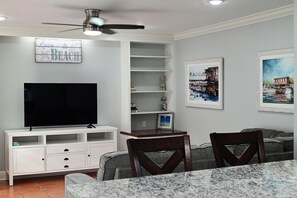 Una sala de estar con televisor de pantalla plana, ventilador de techo, mesa de comedor y dos sillas.
