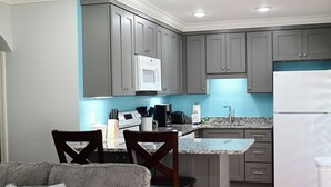 Une cuisine avec des meubles de couleur grise, un micro-ondes blanc, une machine à café et un réfrigérateur.