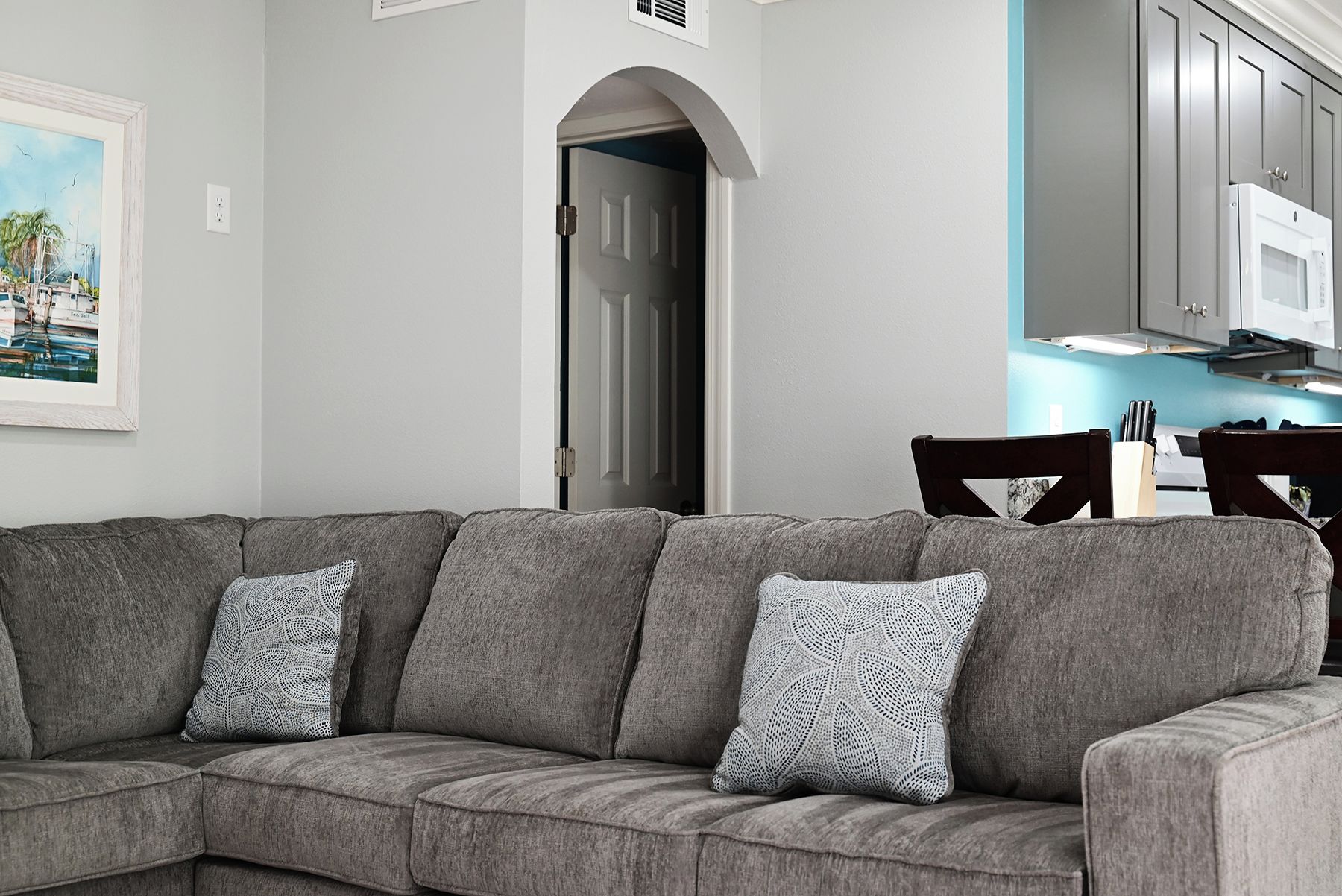 Un sofá seccional gris con cojines estampados en una sala de estar con una puerta blanca y un cuadro en la pared.