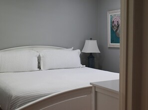 Una cama bien hecha con ropa de cama blanca en una habitación con pared gris y un cuadro en la pared.