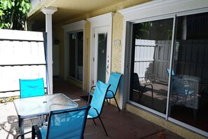 A patio area with a table and chairs, a sliding glass door, and a white fence.