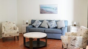 Un salon avec un canapé, deux fauteuils, une table basse et un tableau accroché au mur.