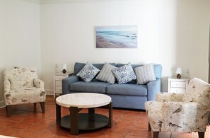 Una sala de estar con un sofá, dos sillones, una mesa de centro y un cuadro en la pared.