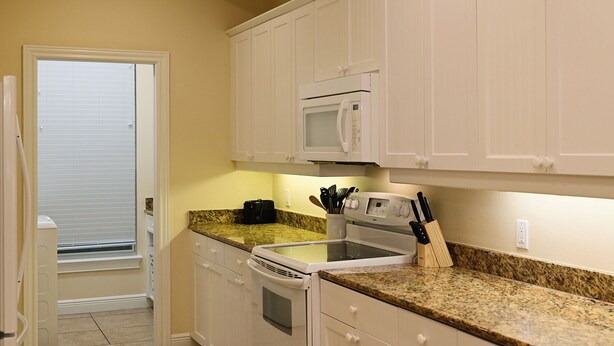 A compact kitchen with white cabinets, a microwave, a stove, and a granite countertop. - Spacious One-Bedroom Condo with Island Comforts (Bradenton Beach)