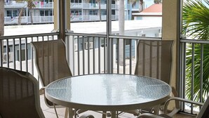 A covered outdoor area with a round table and four chairs, a ceiling fan, and a view of palm trees and buildings.