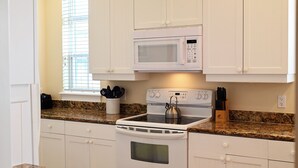 A kitchen with white cabinets, a microwave, a stove, and a kettle.
