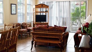 A living room with a large TV, wicker furniture, and a balcony with plants.