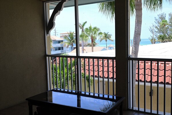 A room with a view of a beach, palm trees, and buildings.