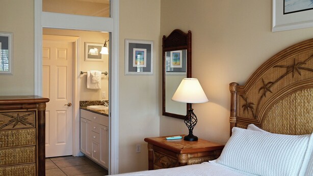 Habitación de hotel con cama, mesita de noche, lámpara, espejo y baño visible a través de una puerta abierta.