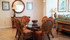 Un coin repas avec une table ronde, des chaises et un miroir. Des tableaux encadrés ornent le mur et une lampe est posée sur la table.