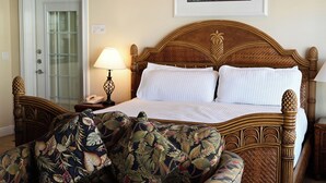 Une chambre d’hôtel avec un lit en bois, une table de chevet avec une lampe, un fauteuil à motifs floraux et une porte dotée d’un panneau en verre dépoli.
