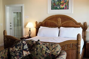 Ein Hotelzimmer mit einem hölzernen Bett, einem Nachttisch mit Lampe, einem stuhl mit Blumenmuster und einer Tür mit Milchglasfenster.