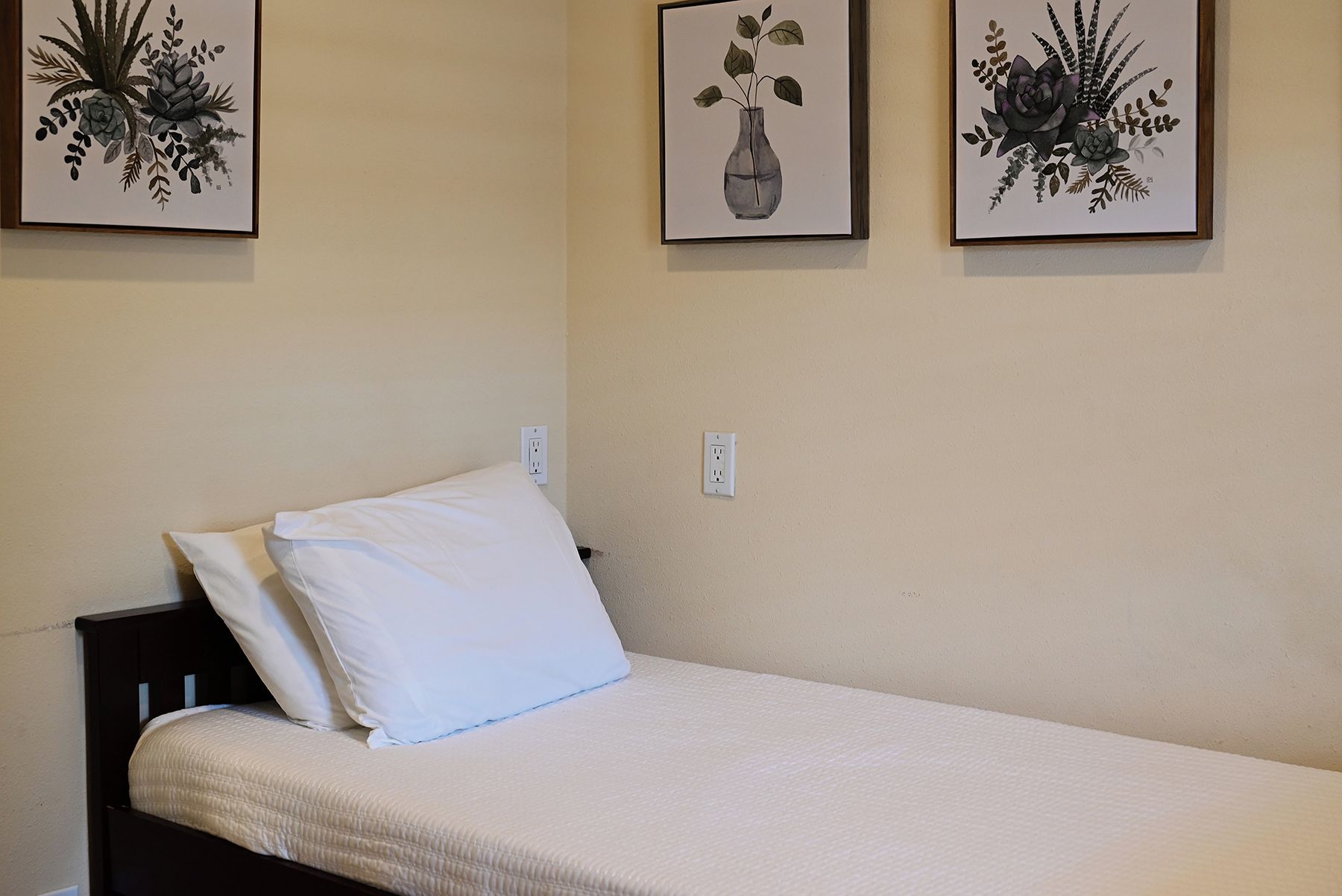 A single bed with white bedding in a room with plain walls.