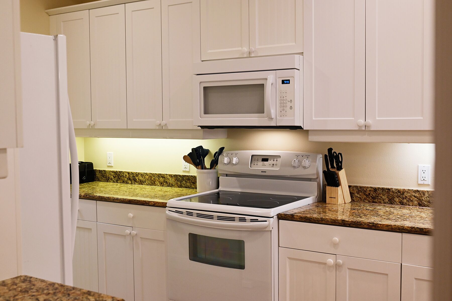 A kitchen with white cabinets, a microwave, an oven, and granite countertops.