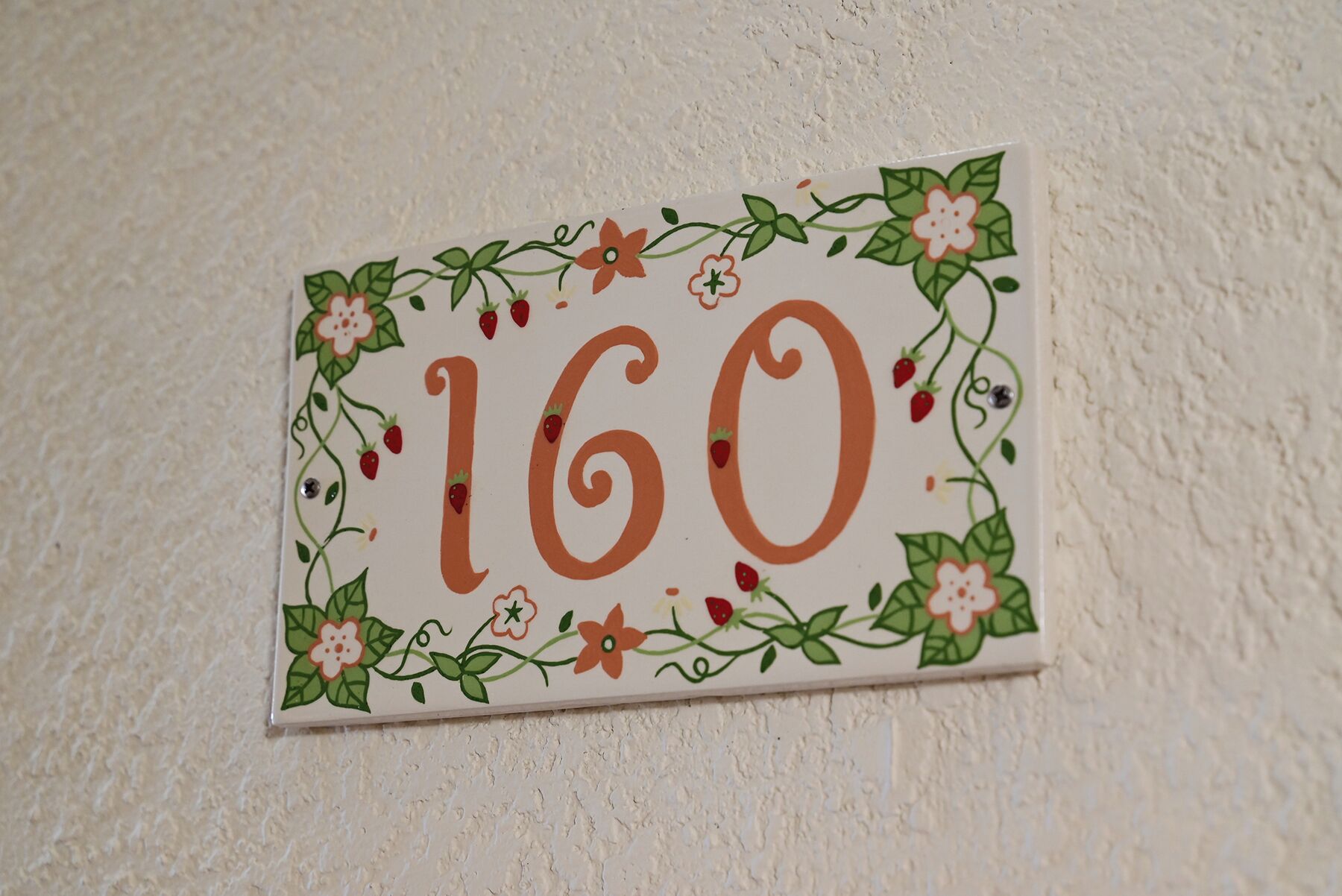 Uma placa fixada na parede com o número '160' rodeado por motivos florais.