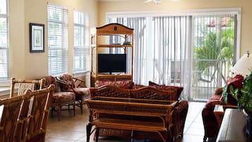 A living room with a large TV, wicker furniture, and a balcony with plants.