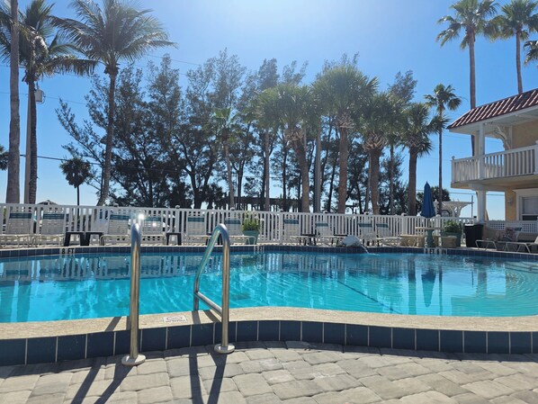 A swimming pool with a white fence, lounge chairs, and palm trees in the background.