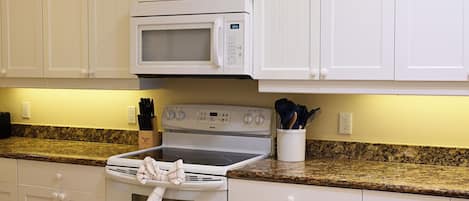 A kitchen with white cabinets, a microwave, a stove, and granite countertops.