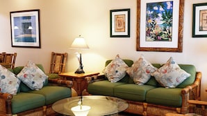 Una habitación con un sofá verde, cojines a juego, una mesa de centro de vidrio y cuadros en las paredes.