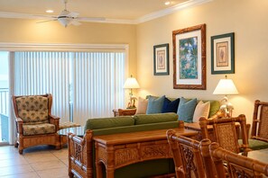 A room with a bed, two armchairs, a wooden table, and a ceiling fan.