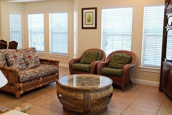 A living room with a patterned sofa, two armchairs, a glass coffee table, and a framed picture on the wall.