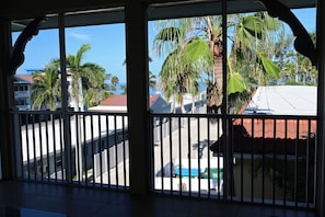 A balcony with metal railings, a view of palm trees, and a building with a red roof.