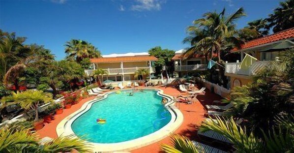 A resort with a central swimming pool surrounded by palm trees and lounge chairs.