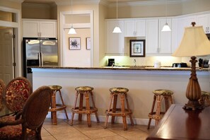Una cocina con armarios blancos, un refrigerador, una cafetera y un taburete de bar.