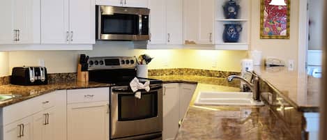 Una cocina moderna con armarios blancos, electrodomésticos de acero inoxidable, encimera de granito y un salpicadero decorativo.