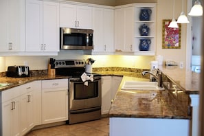 Una cocina moderna con armarios blancos, electrodomésticos de acero inoxidable, encimera de granito y un salpicadero decorativo.