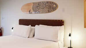 A hotel room with a bed, pillows, a headboard, a wall-mounted artwork, a bedside lamp, and a red object on the nightstand. - Convenient Ground-Floor Room Steps from the Beach (Bradenton Beach)