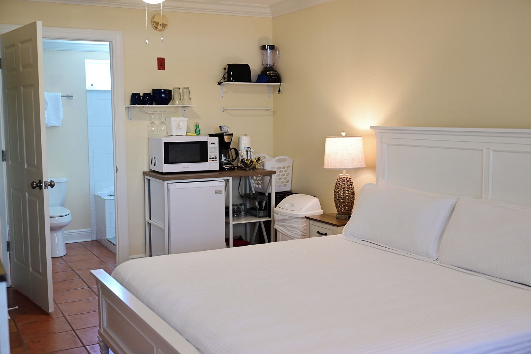 Une chambre d’hôtel comprenant un lit, un bureau avec un micro-ondes, une lampe et un espace douche.