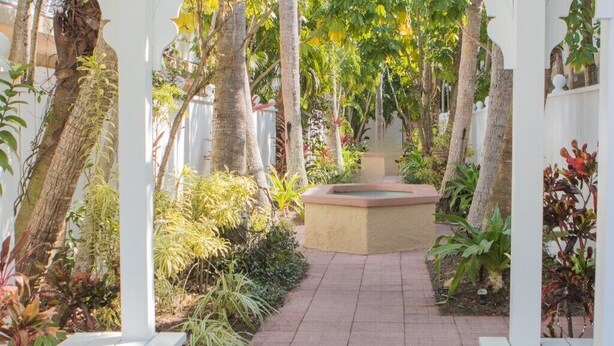 Un sendero en el jardín con bancos blancos y una jardinera central.