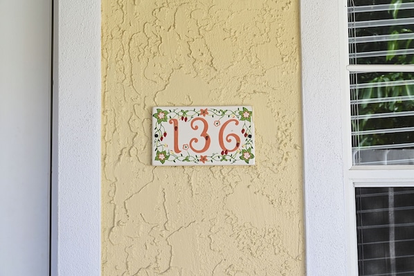 A house number plaque with floral design on a textured wall.