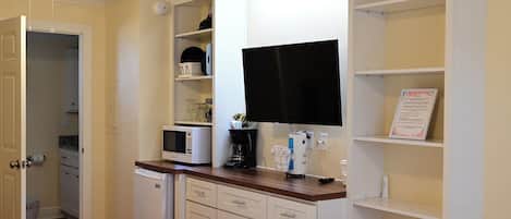 A hotel room with a bed, a flat-screen TV mounted on the wall, a microwave, a coffee maker, and a small refrigerator.