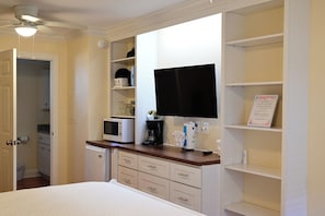 A hotel room with a bed, a flat-screen TV mounted on the wall, a microwave, a coffee maker, and a small refrigerator.