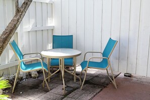 Eine Terrasse mit einem runden Tisch und vier Stühlen, einem weißen Zaun und einem Baum.
