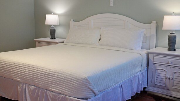 Una cama impecable con cabecera y piecera blancos, flanqueada por dos mesitas de noche con lámparas.