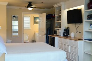 Un dormitorio con cama, ventilador de techo, baño con inodoro y kitchenette con microondas.