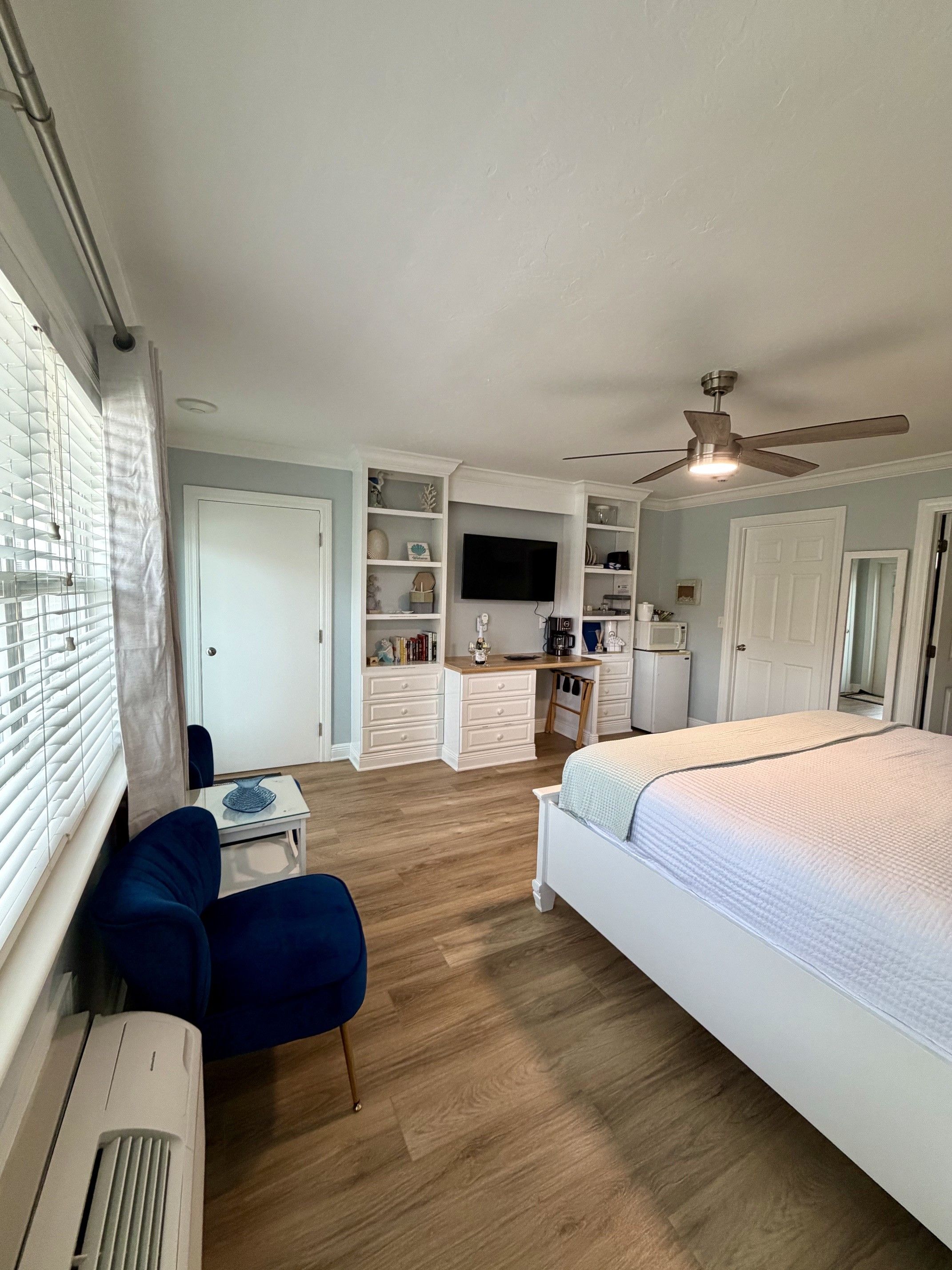 A bedroom with a bed, a desk, and a chair. There is a television mounted on the wall.