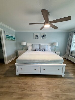 A bedroom with a bed, nightstands, a ceiling fan, and artwork on the walls. - 248B: Anna Maria Island , King Room, Steps from the beach (Bradenton Beach)