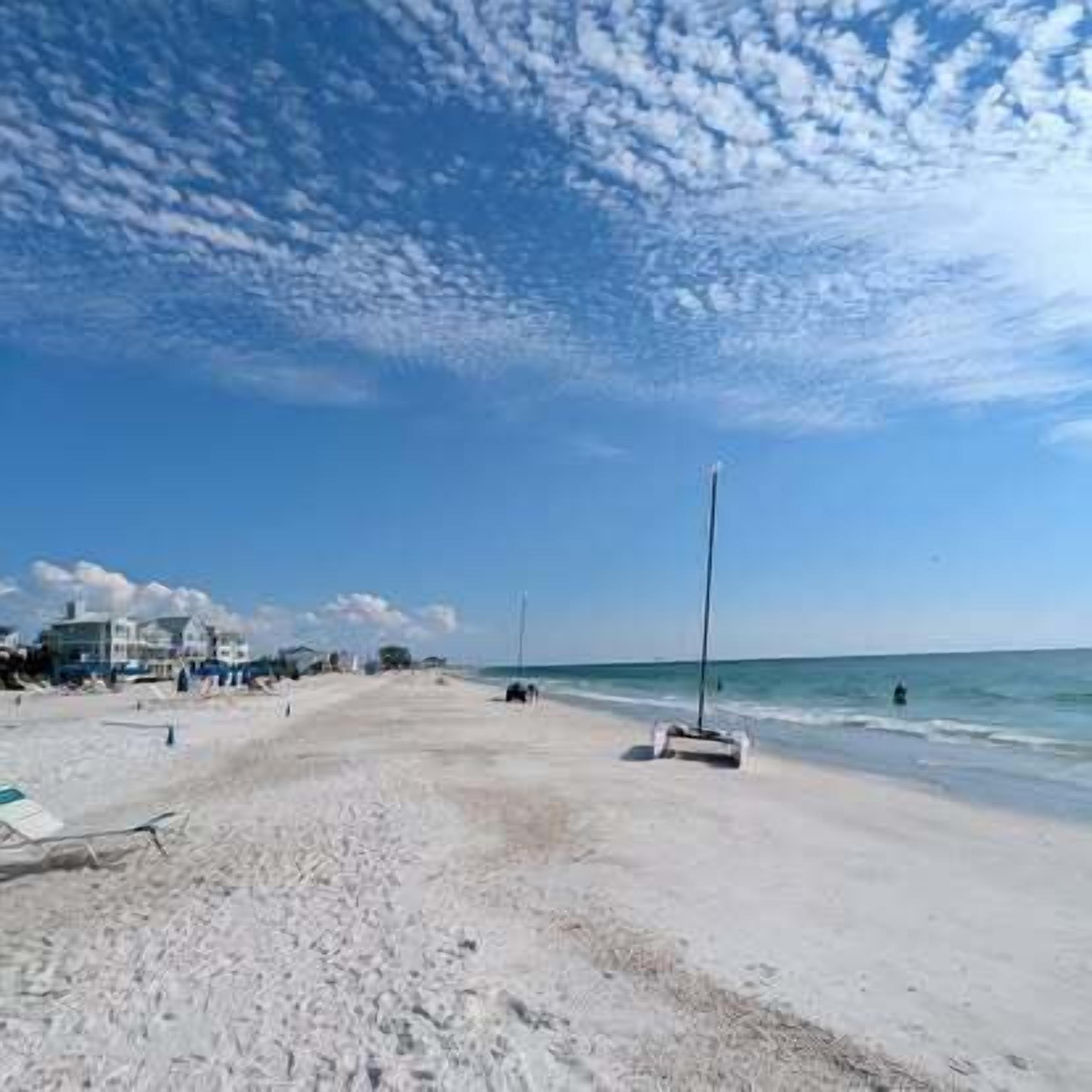 A beach with a clear sky, a sandy shore, and a few buildings in the background.