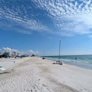 Ein Strand mit blauem Himmel, sandigem Ufer und einigen Gebäuden im Hintergrund.