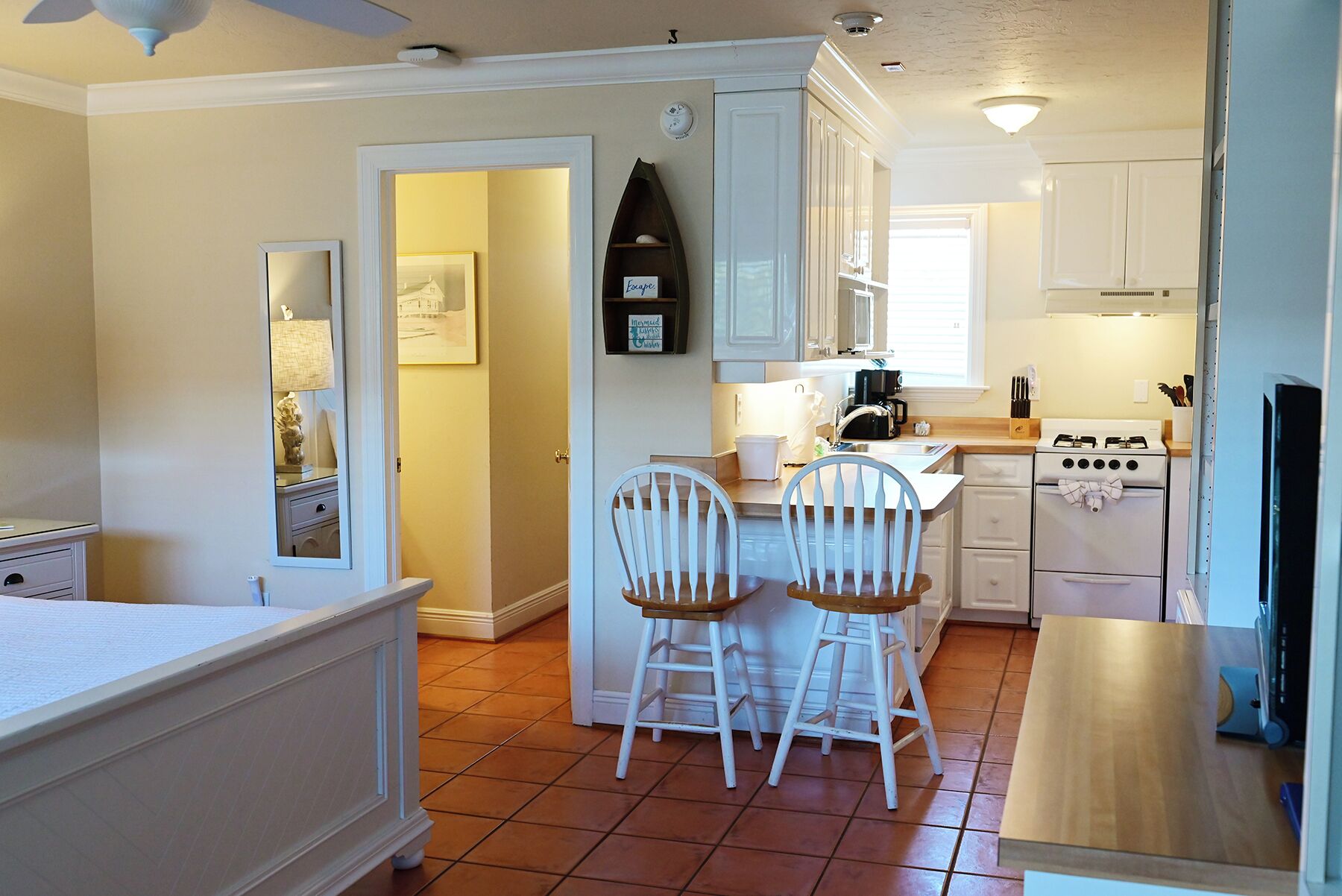 A compact kitchen with white cabinets, a stove, and two bar stools.