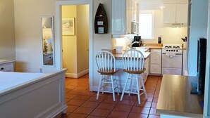 A compact kitchen with white cabinets, a stove, and two bar stools. - Bright Second-Floor Studio Near the Beach (Bradenton Beach)