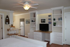 Un dormitorio con cama, escritorio, silla, televisor y estanterías empotradas con libros y adornos.