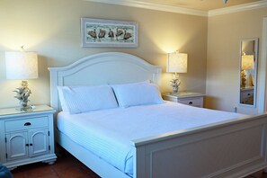 A neatly made bed with white bedding, two bedside tables with lamps, a wall-mounted mirror, and a framed picture above the bed. - Bright Second-Floor Studio Near the Beach (Bradenton Beach)