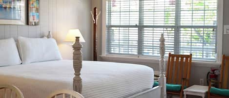 Ein Schlafzimmer mit einem Bett, einem Nachttisch, einer Lampe, einem Stuhl und einem Fenster mit Jalousien.
