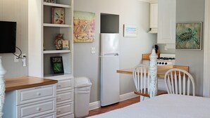 Een praktische keuken met witte kasten, een koelkast, een fornuis, en een eethoek met een stoel en tafel.